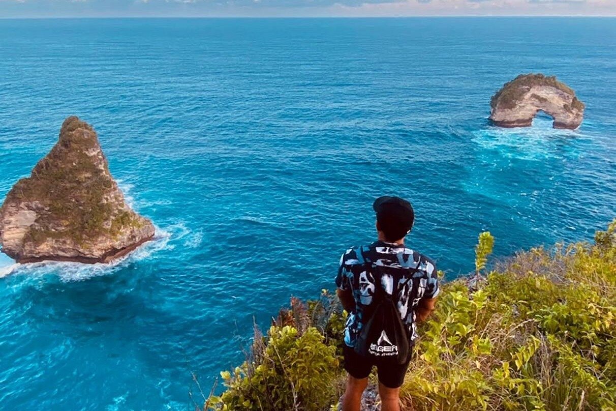 Solo traveller looking out at the natural sea arch from a cliff