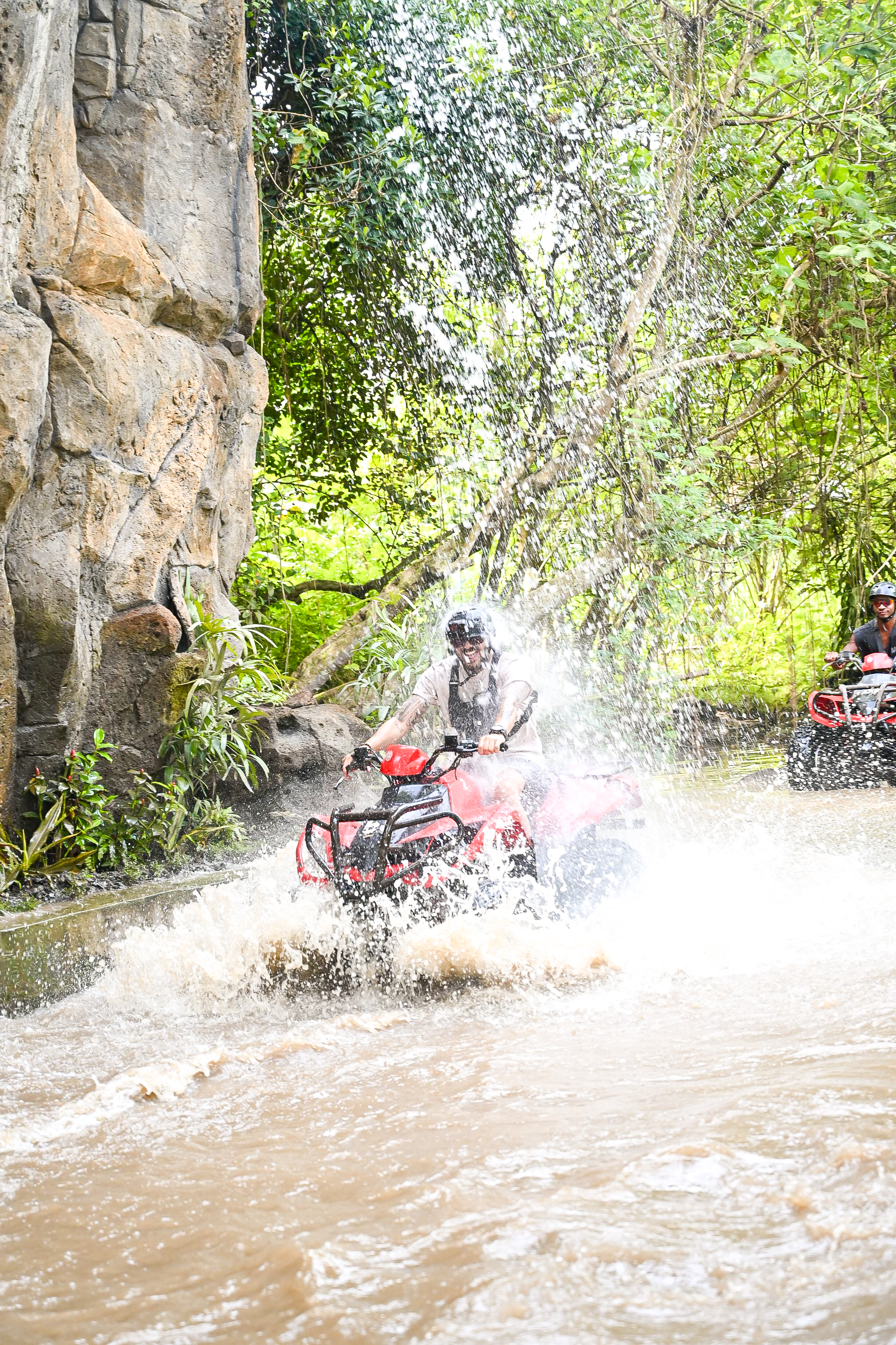 Rider crossing a jungle waterfall with ATV mid-spray